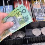 Cash flow management small business course - Photo of an open cash register with a hand inserting two $100 notes in Australian dollars