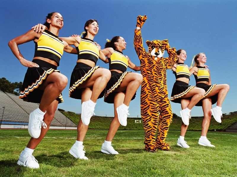 A team of 5 cheerleaders and a tiger mascot cheer on a field