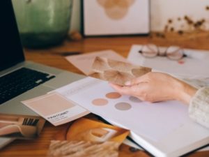 Create a brand style guide in Canva - photo of a womans hand sorting through colour palettes on a desk near a laptop