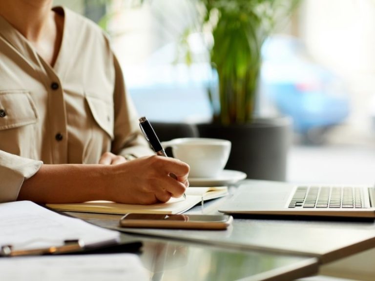 How to write a good blog post - photo of a woman writing on a notepad in front of her laptop