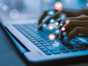 How to write social media captions for small business - hads typing on a keyboard. graphics of social media 'likes' and 'hearts' overlaid on top