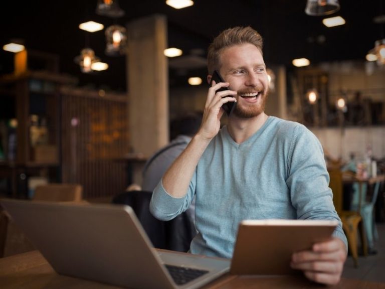 Man on the phone while sitting at his laptop, hiring a marketing freelancer