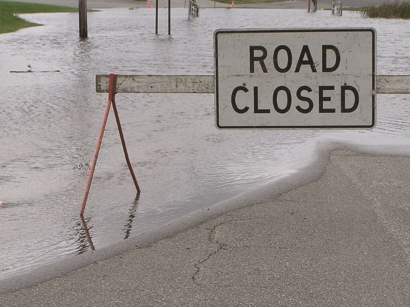 Photo of a road partially covered with water and a sign that says "road closed"